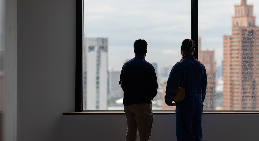 Two people in silhouette standing in front of a large window looking out at the downtown skyline in the distance