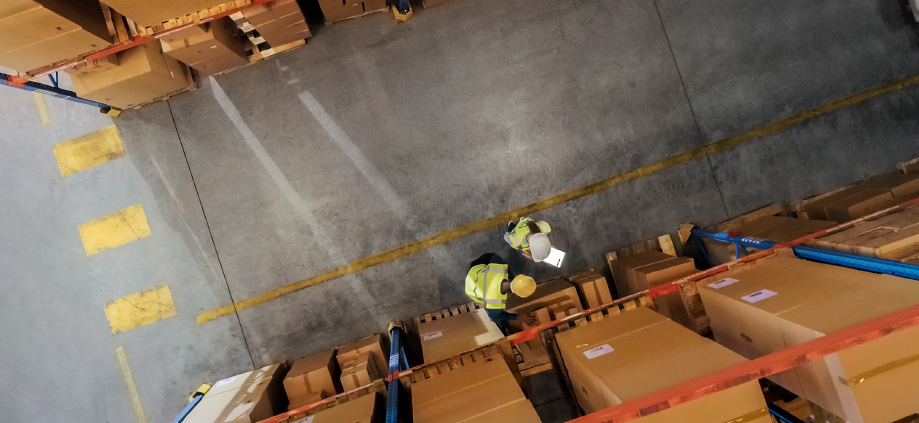 Two workers in hard hats inspect boxes in an industrial facility. 