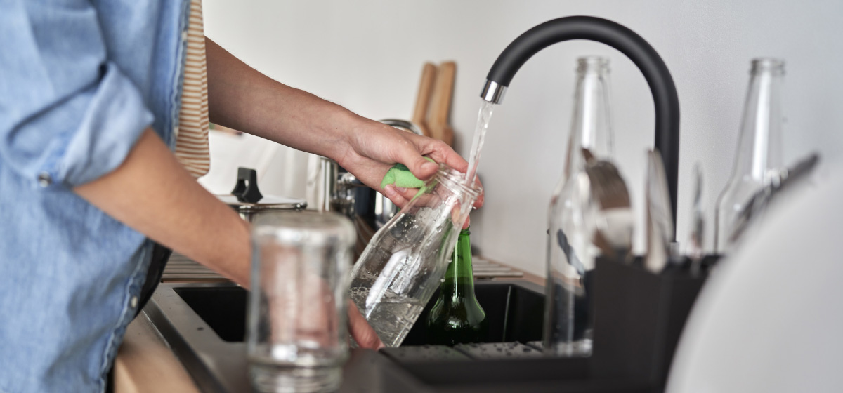 Glass bottle being washed under a kitchen sink faucet