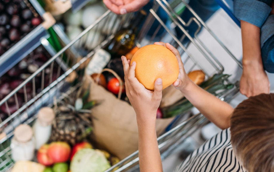 A child puts fruit into a grocery cart.  