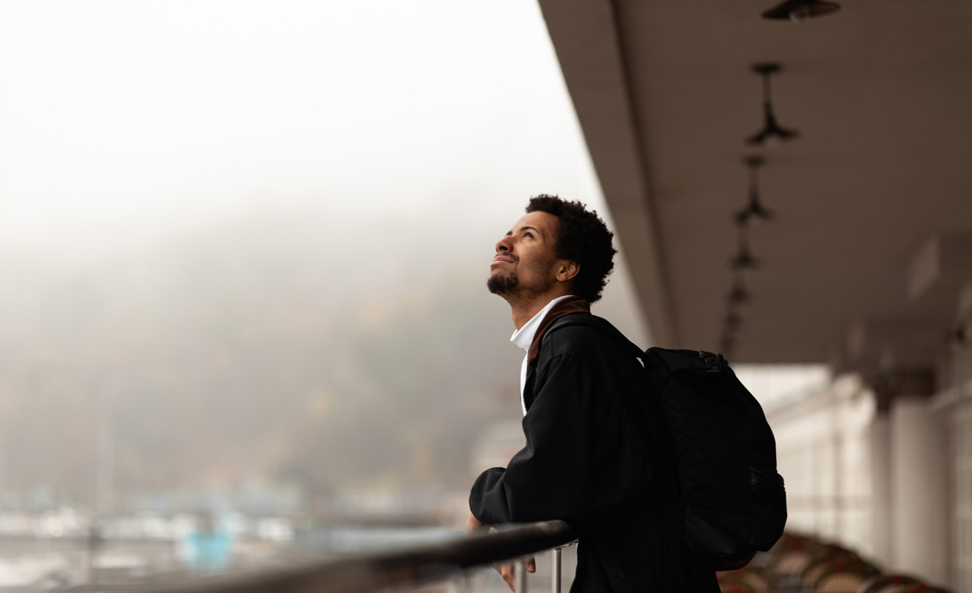 A man leaning on a balcony rail looking up at a grey sky