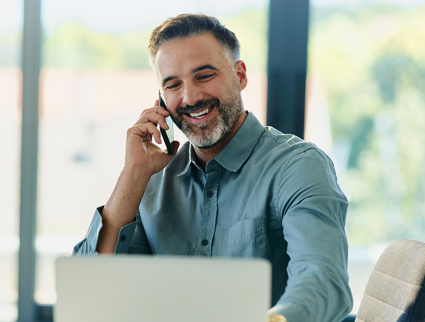 Man smiling while talking on phone at laptop