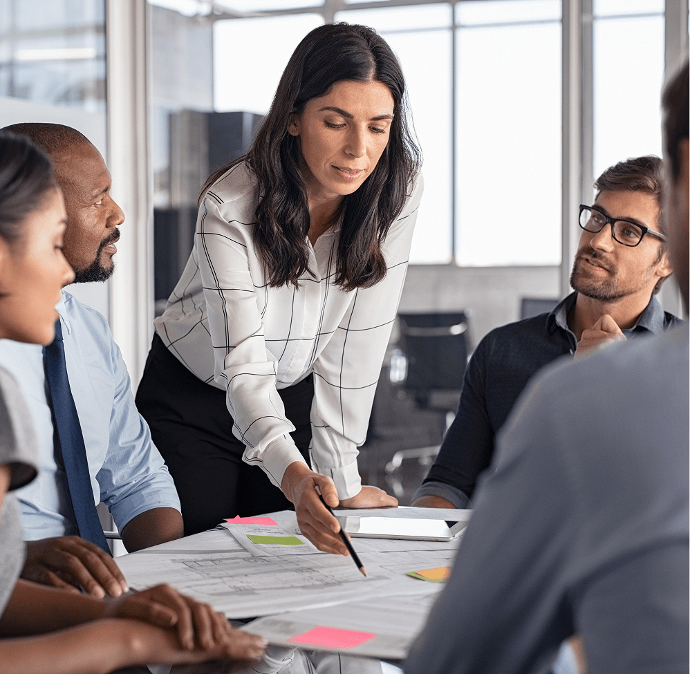 Woman standing and pointing to paper in meeting with colleagues