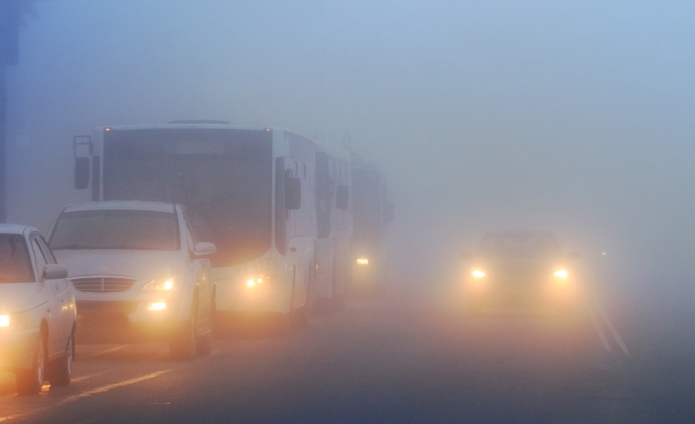 Cars driving through the fog down a two-lane road